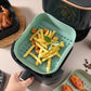 A hand sets a mint green silicone liner tray of crinkle fries into an air fryer basket