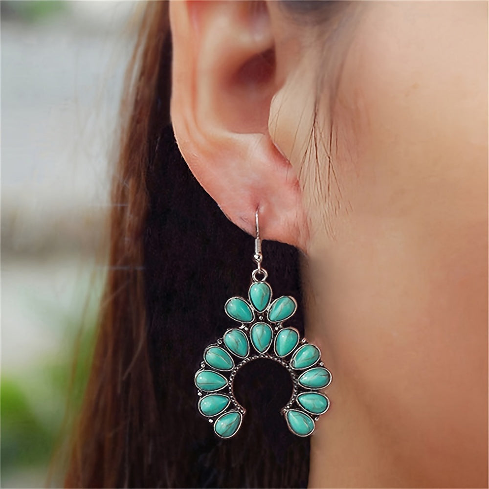 Close up of a woman's ear wearing a crescent drop earring with turquoise colored teardrop stones