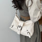 White soft vegan leather hobo bag with front buckle strap worn over the shoulder with a grey dress