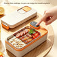 Cream and orange electric lunch box with a finger on the display button and rice and sausages in the steel liner