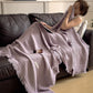 Lilac Purple cotton gauze throw blanket with tassel fringe, draped over a seated woman on a dark leather sofa, view 3 of 4