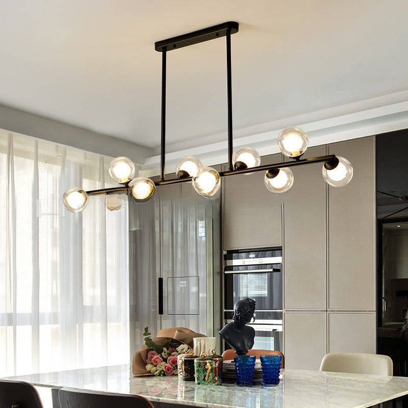 Black linear pendant light with six glass globe shades hanging over a marble kitchen island and dining area