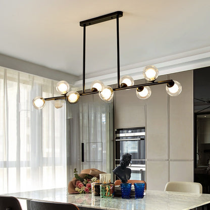 Black linear pendant light with six glass globe shades hanging over a marble kitchen island and dining area