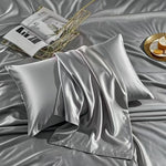 Silver gray satin finish polyester pillowcases styled on a bed with a magazine