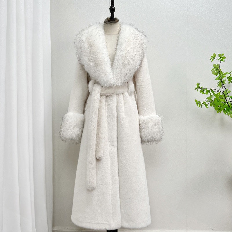 White long belted vegan fur coat with a wide fur collar and fur cuffs on a mannequin beside a plant