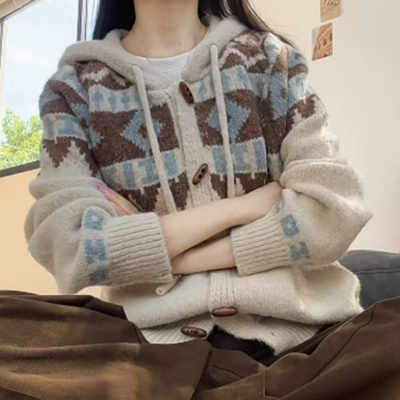 Cream hooded cardigan with brown and blue yoke, ribbed cuffs and sleeve motif, arms crossed