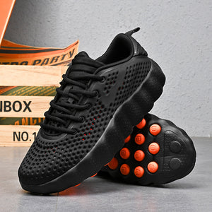 Black and orange running shoe standing beside its studded massage outsole