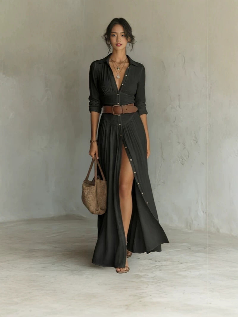Woman in a black long shirt dress with collar, brown belt and a high front slit, full length front view