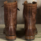 Back view of two brown lace-up boots with stitched heel counters and stacked heels, gallery photo