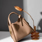 Khaki leather bucket bag styled on table with dried flower and glass vase