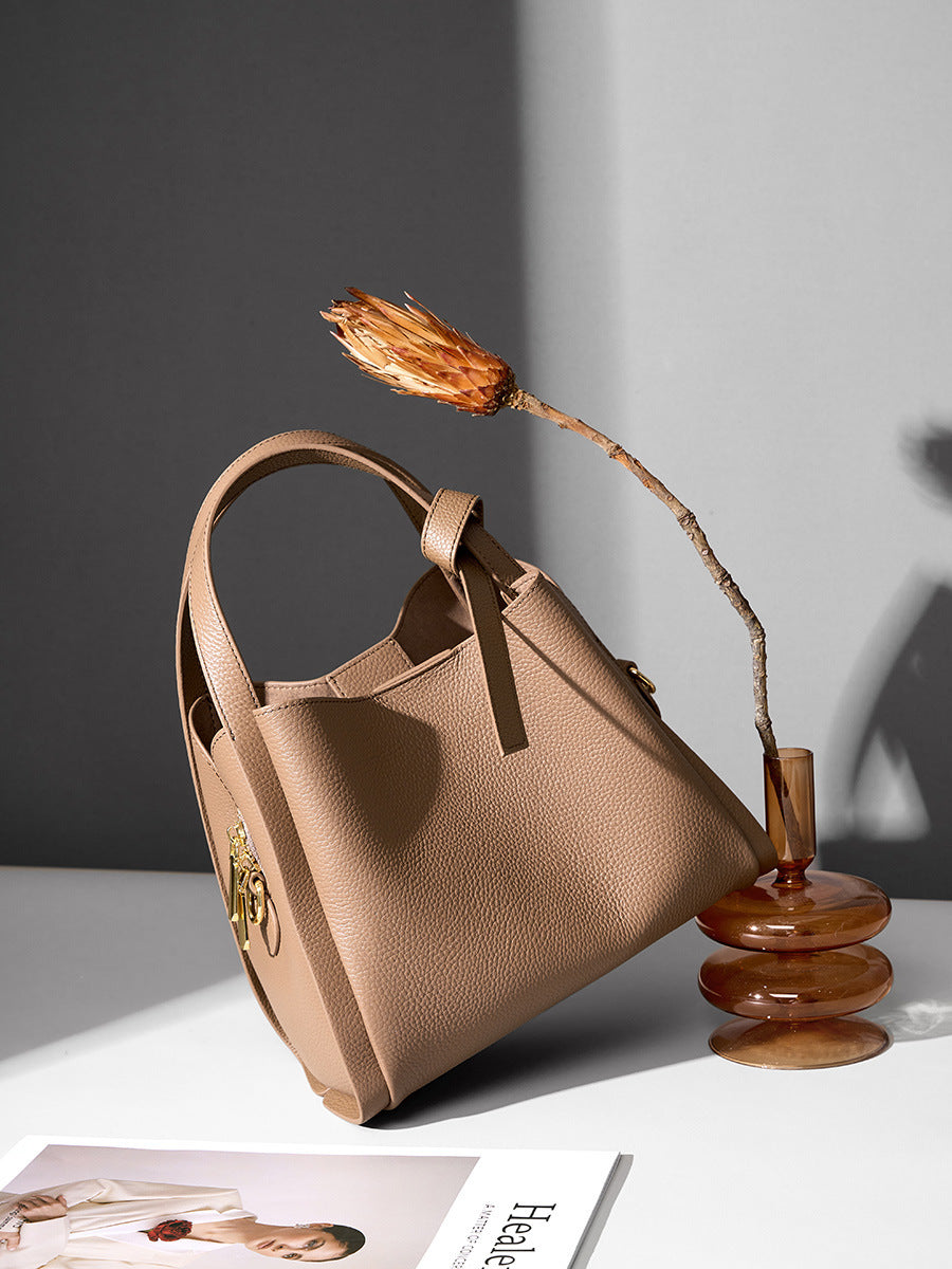 Khaki leather bucket bag styled on table with dried flower and glass vase