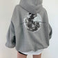 Light gray oversized hooded sweatshirt seen from behind with a large grayscale moon print across the back