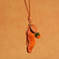 Tan orange peanut shaped leather pendant hanging from a knotted cord with an orange glass bead and round stamped tag