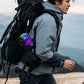 Hiker with the small iridescent speaker hooked onto a backpack strap outdoors