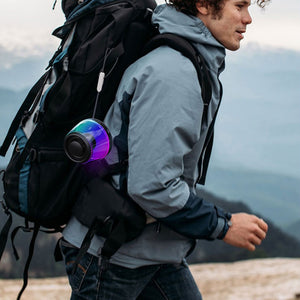 Hiker with the small iridescent speaker hooked onto a backpack strap outdoors