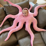 Child wearing the pink octopus plush costume with tentacles spread across a sofa