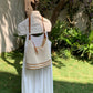 Woman carrying a cream open weave shoulder bag crossbody on a garden bench