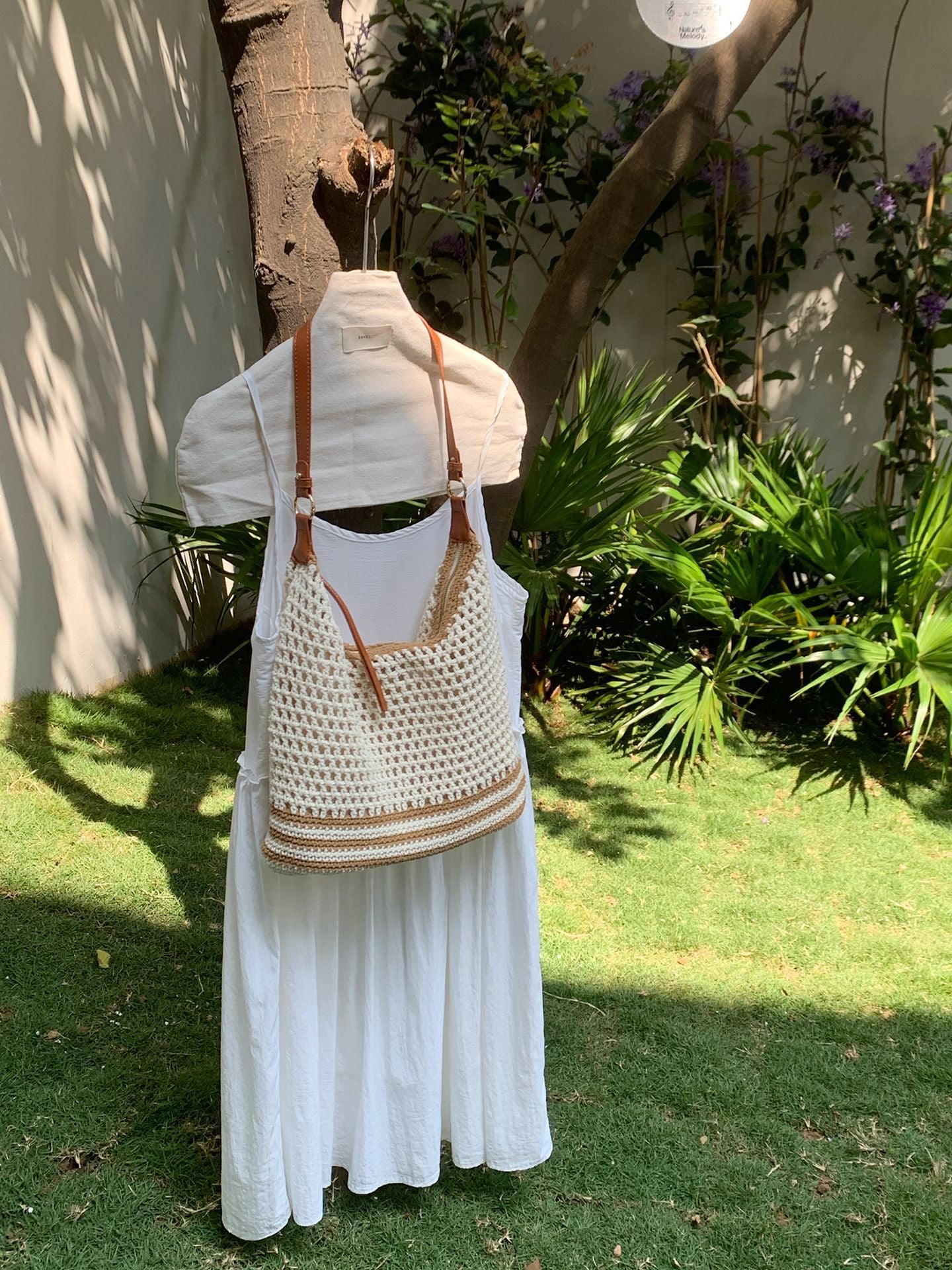 Woman carrying a cream open weave shoulder bag crossbody on a garden bench