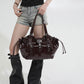Woman holding a glossy dark coffee brown hobo shoulder bag by its strap, with buckle straps and drawstring sides