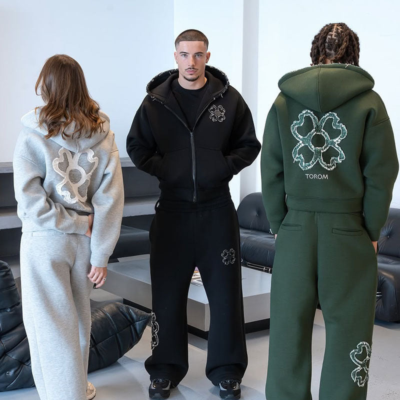 Gray hoodie back with clover motif, black zip hoodie front and green hoodie back in a lounge setting