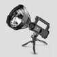 Black portable LED searchlight standing on its folding tripod bracket with USB charging handle
