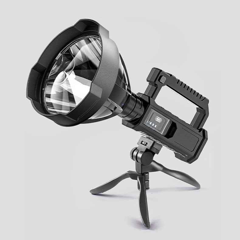 Black portable LED searchlight standing on its folding tripod bracket with USB charging handle