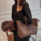 Woman in a black blazer carrying a brown PU tote on her shoulder and a small brown pouch in her hand