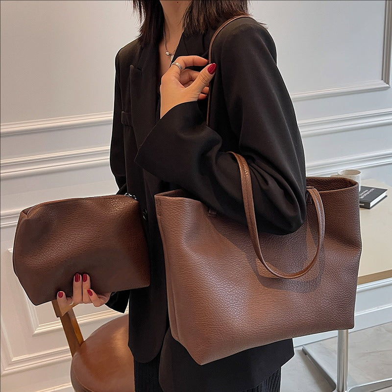 Woman in a black blazer carrying a brown PU tote on her shoulder and a small brown pouch in her hand