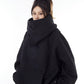 Black oversized hooded sweatshirt with the tall stand collar pulled up and a hand in the front pocket, size option L