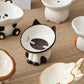 Siamese cat shaped raised ceramic bowl on a woven mat next to panda and other ceramic bowls