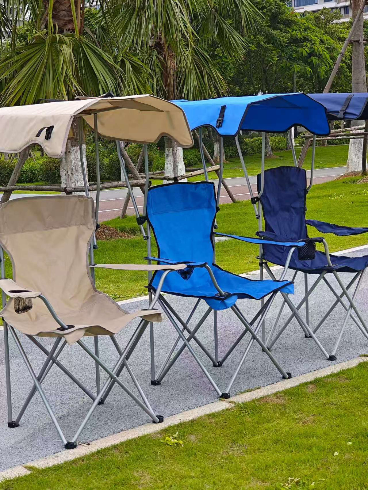 Three foldable camping chairs with canopies in beige, blue and navy lined up on a park path