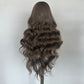 Back view of a long wavy gray brown synthetic wig on a mannequin against a light wall