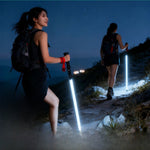 Two women night hiking on a dark trail, each holding a glowing white LED trekking pole