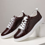 Pair of burgundy crocodile embossed low-top sneakers with white laces and a thick white sole on white blocks