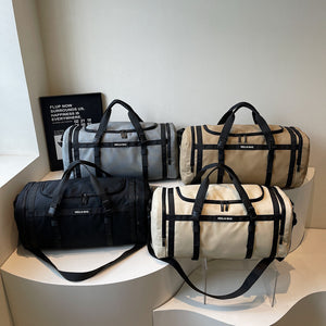 Four travel duffel bags in gray, khaki, black and ivory displayed together on white risers
