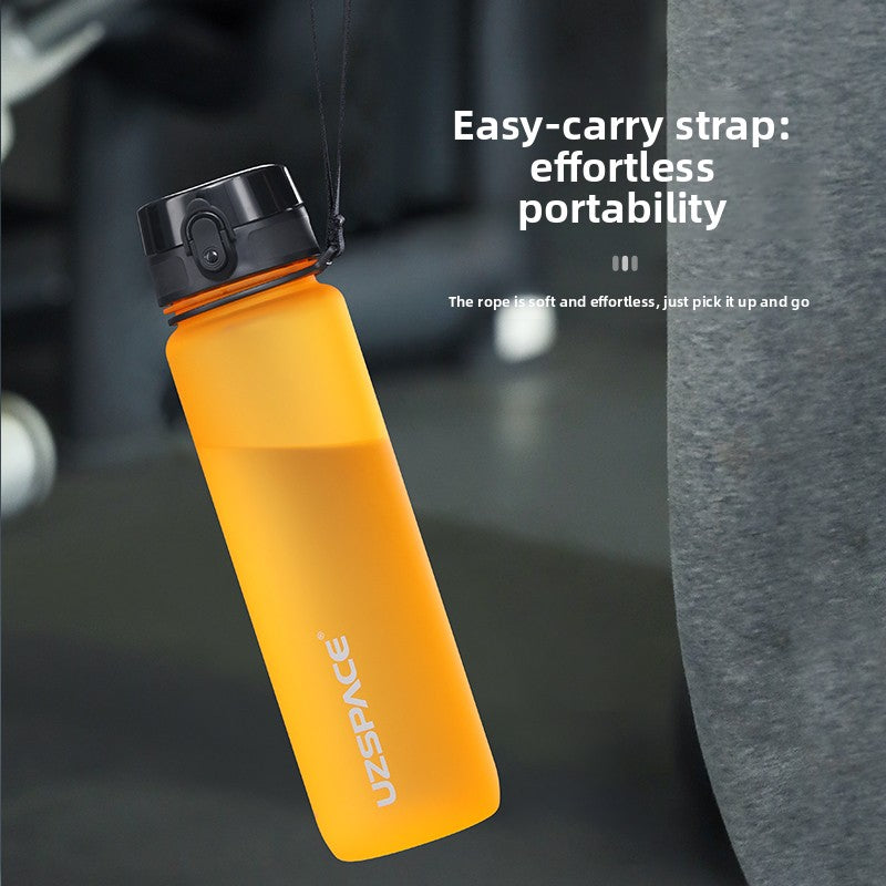Orange sports water bottle hanging by its soft black carry cord in a gym