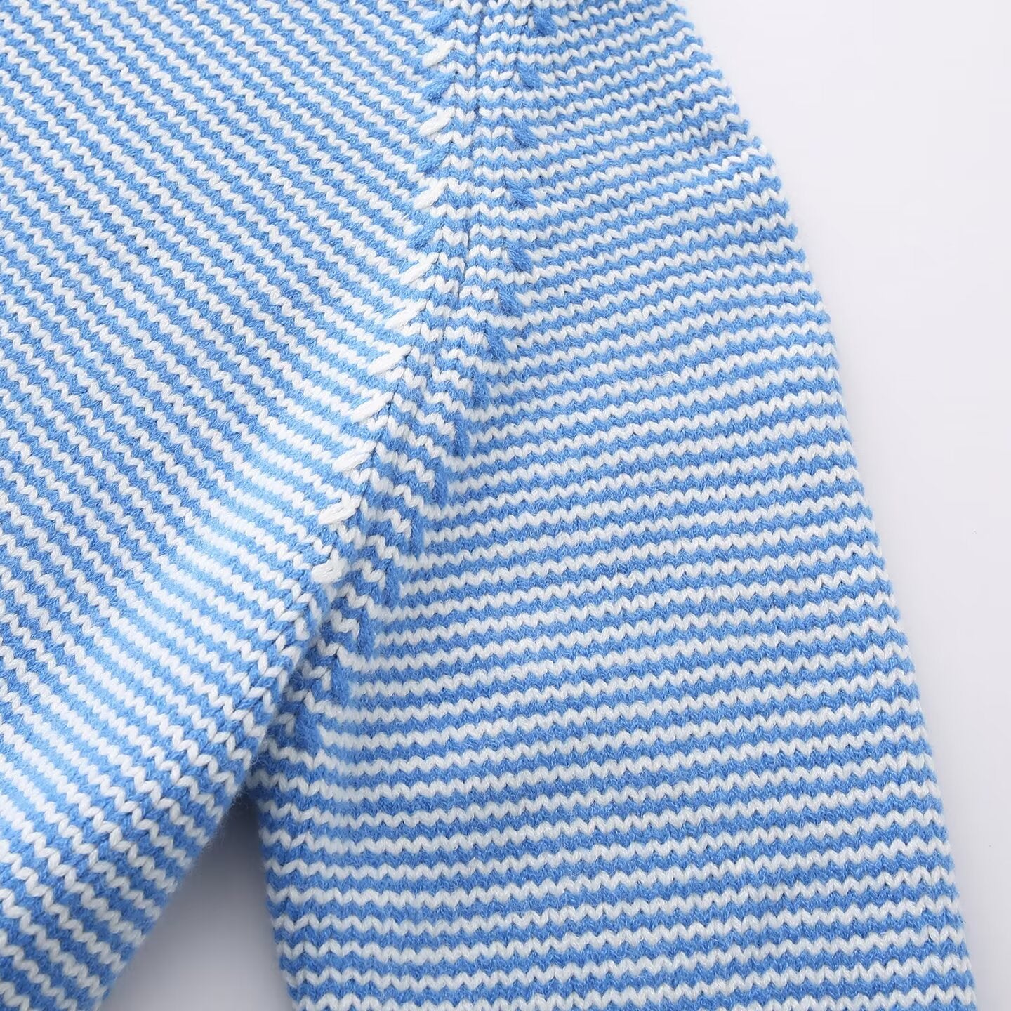 Hand holding the striped knit sweater hem to show ribbed edge and knit scale