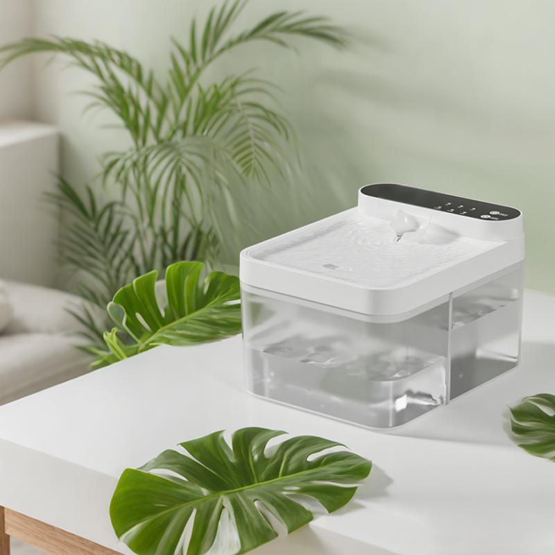 White and clear pet water fountain on a wooden table next to green plant leaves in a bright room