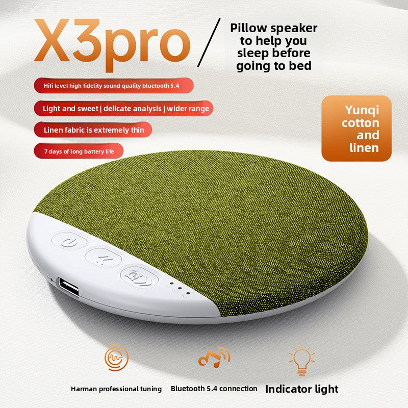 Green fabric pillow speaker lying on pale bedding beside a pillow edge