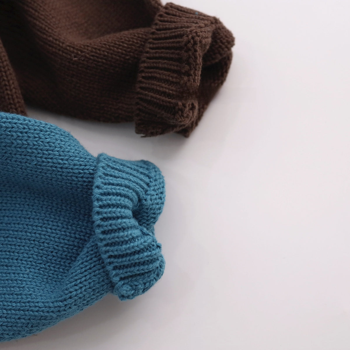 Close up of ribbed cuffs on a blue and a brown cotton knit sweater