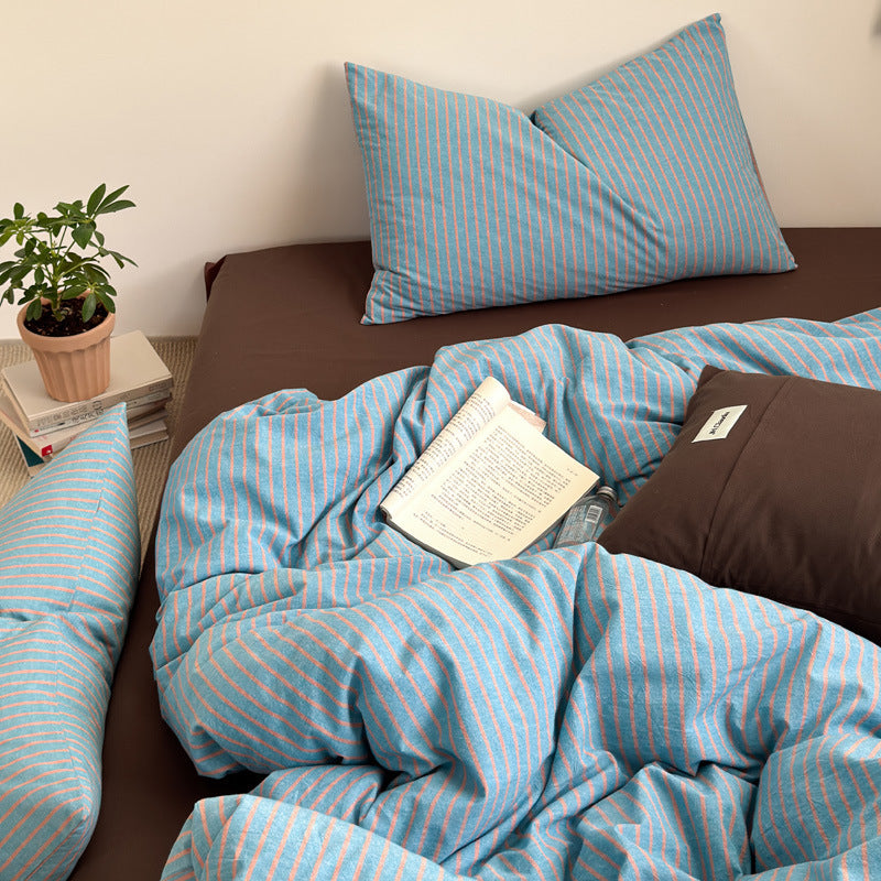 Close view of a blue and coral striped cotton quilt cover and pillow with a brown pillowcase on the bed
