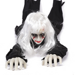 White-haired female ghost prop in tattered black clothes crawling forward with pale plastic hands, front view