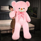 Tall pink plush teddy bear with a pink striped bow tie held by a woman in a bedroom