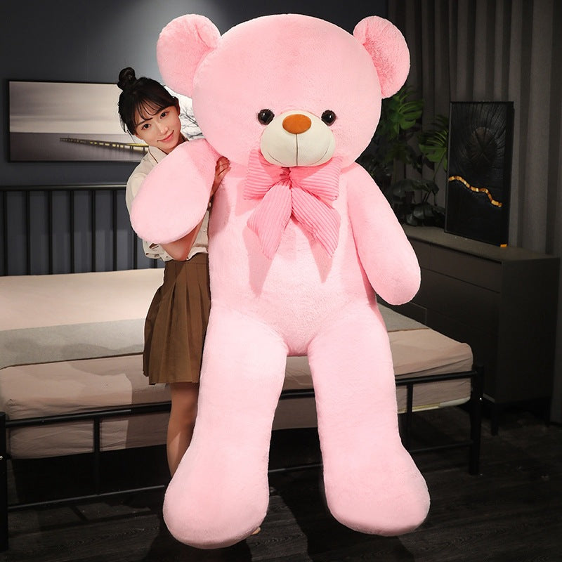 Tall pink plush teddy bear with a pink striped bow tie held by a woman in a bedroom