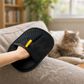 Black two-way fur removal mitt with yellow tab resting on a sofa with a cat