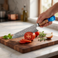 Damascus chef knife slicing a ripe tomato cleanly on a wooden board in a bright kitchen