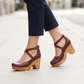 Woman walking on a city pavement wearing the burgundy chunky wooden heel cross strap sandals