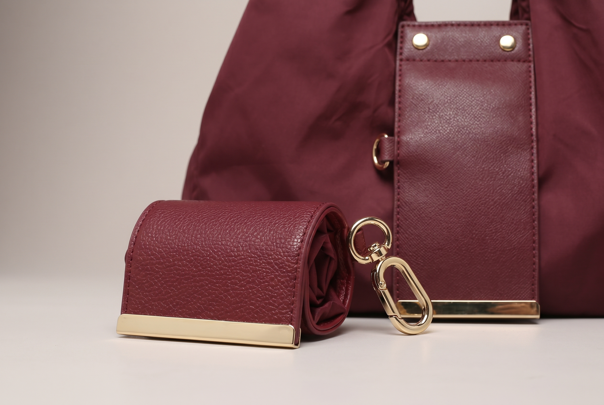 Close up of burgundy leather mini pouch charm with gold lobster clasp and metal bar