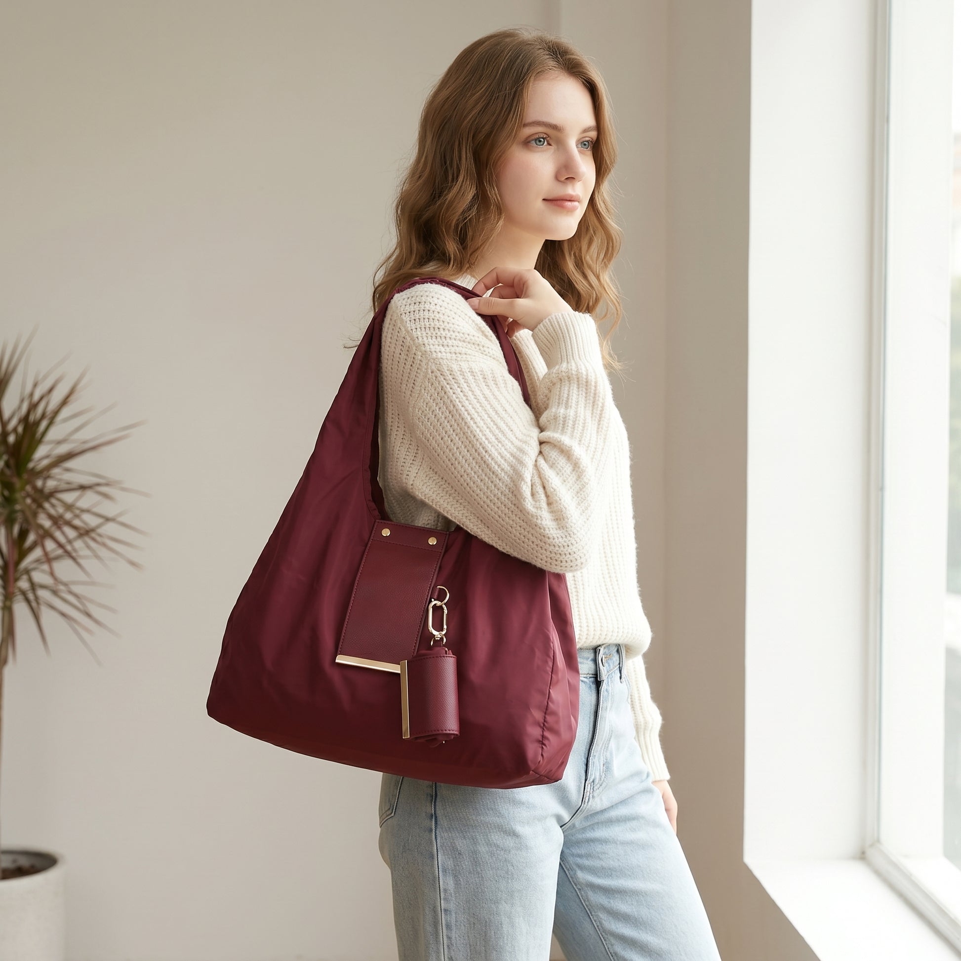 Woman carrying the burgundy nylon tote with mini pouch charm over her shoulder