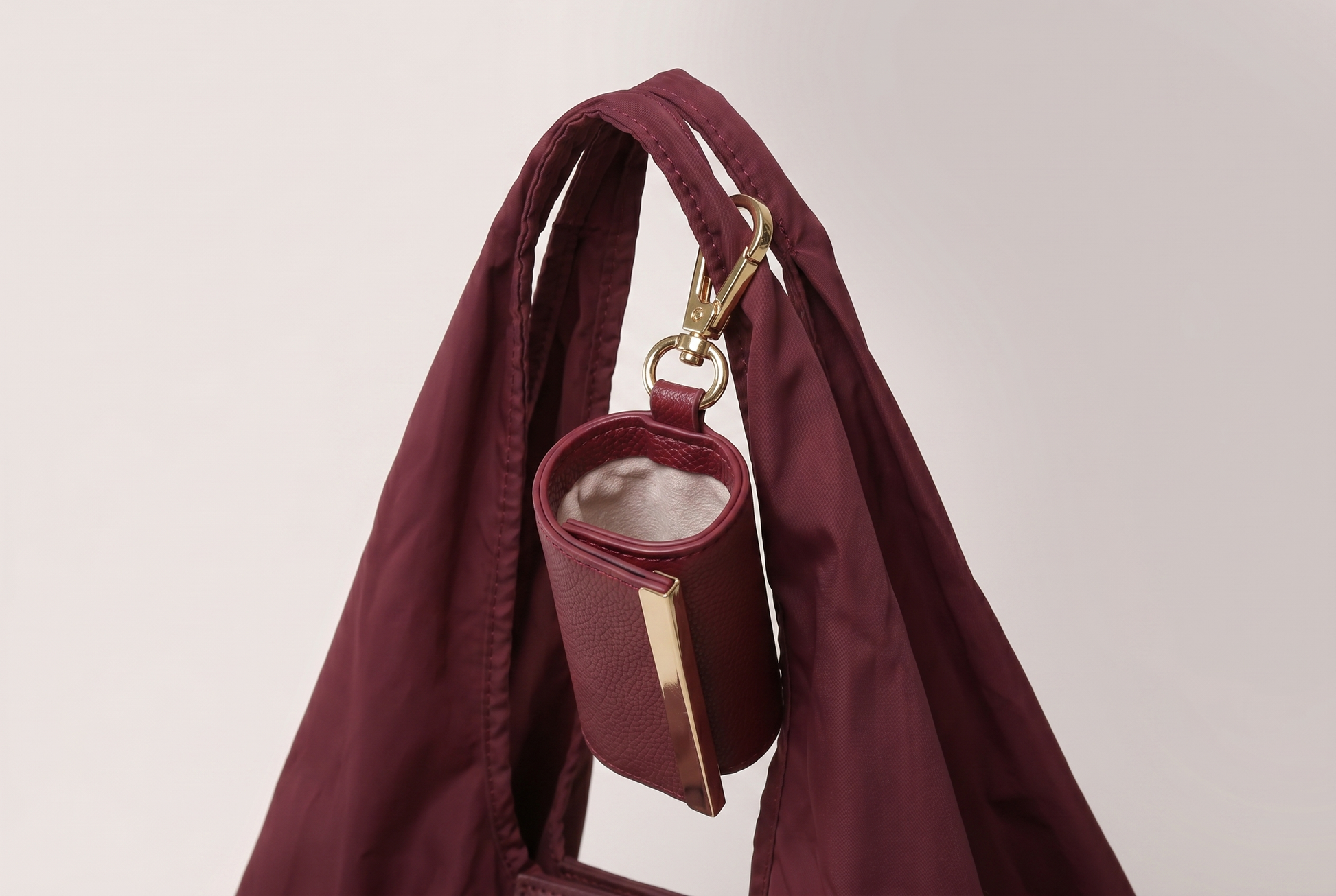 Burgundy leather mini pouch charm clipped to the handle of the nylon tote open top view